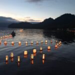 ※写真は、十和田湖畔休屋地区で毎年お盆明けに行われている灯ろう流しです。湖水まつり当日は、手漕ぎボートで願いが書き込まれた灯ろうをけん引します。