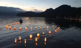 ※写真は、十和田湖畔休屋地区で毎年お盆明けに行われている灯ろう流しです。湖水まつり当日は、手漕ぎボートで願いが書き込まれた灯ろうをけん引します。