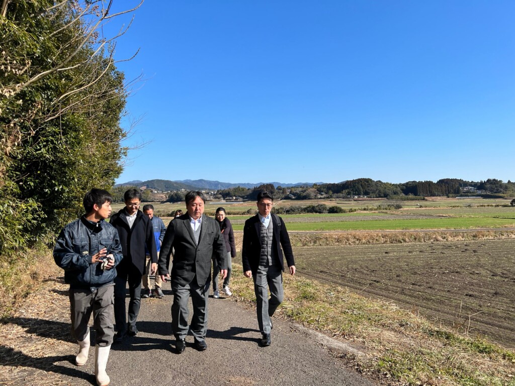 視察の様子、後ろに広がるのは自社栽培の畑