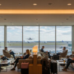 ANA「1万円割引クーポン」活用術をテーマに、空港ラウンジでくつろぐ旅行者たちの様子を描いた画像です。
